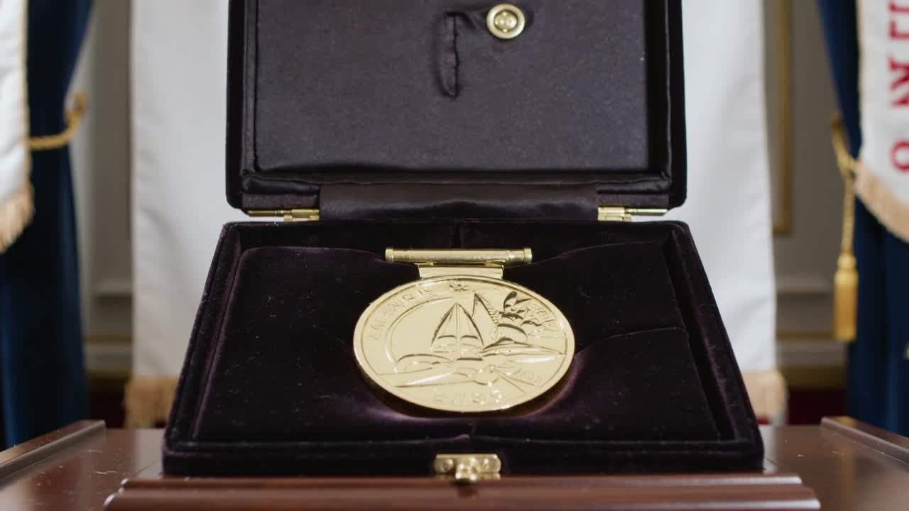 Lid lifting revealing gold medal with sailboat engraving in velvet case on lectern, for award