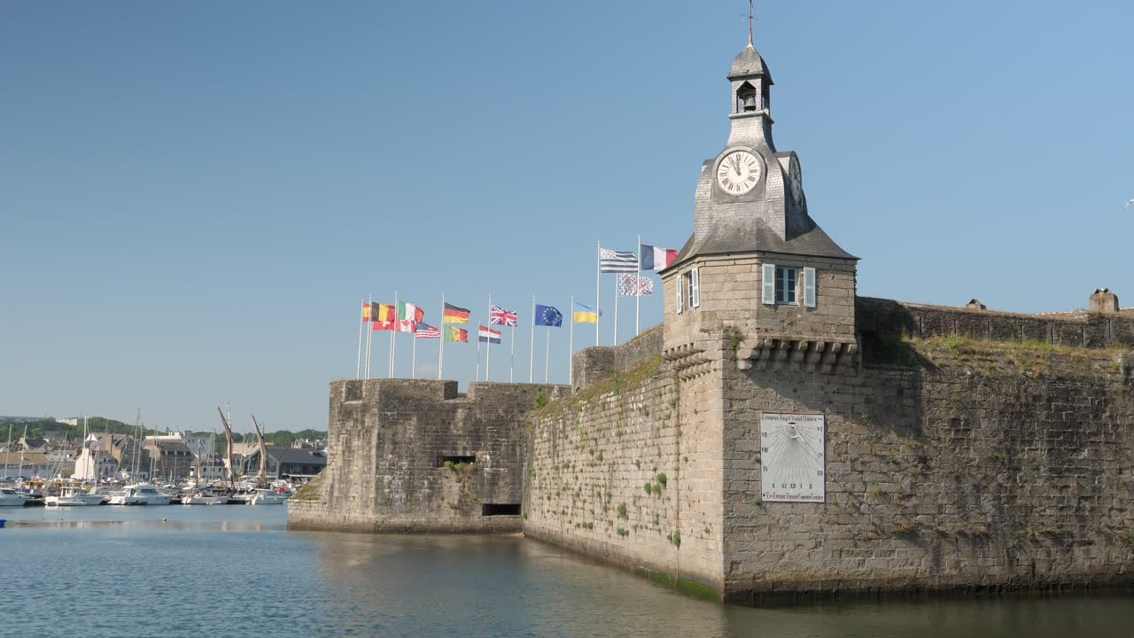 Statisk bilde på en lys solrik dag som viser internasjonale flagg som vaier over den middelalderske murbefestede byen Concarneau, Bretagne, Frankrike, med havn i bakgrunnen.