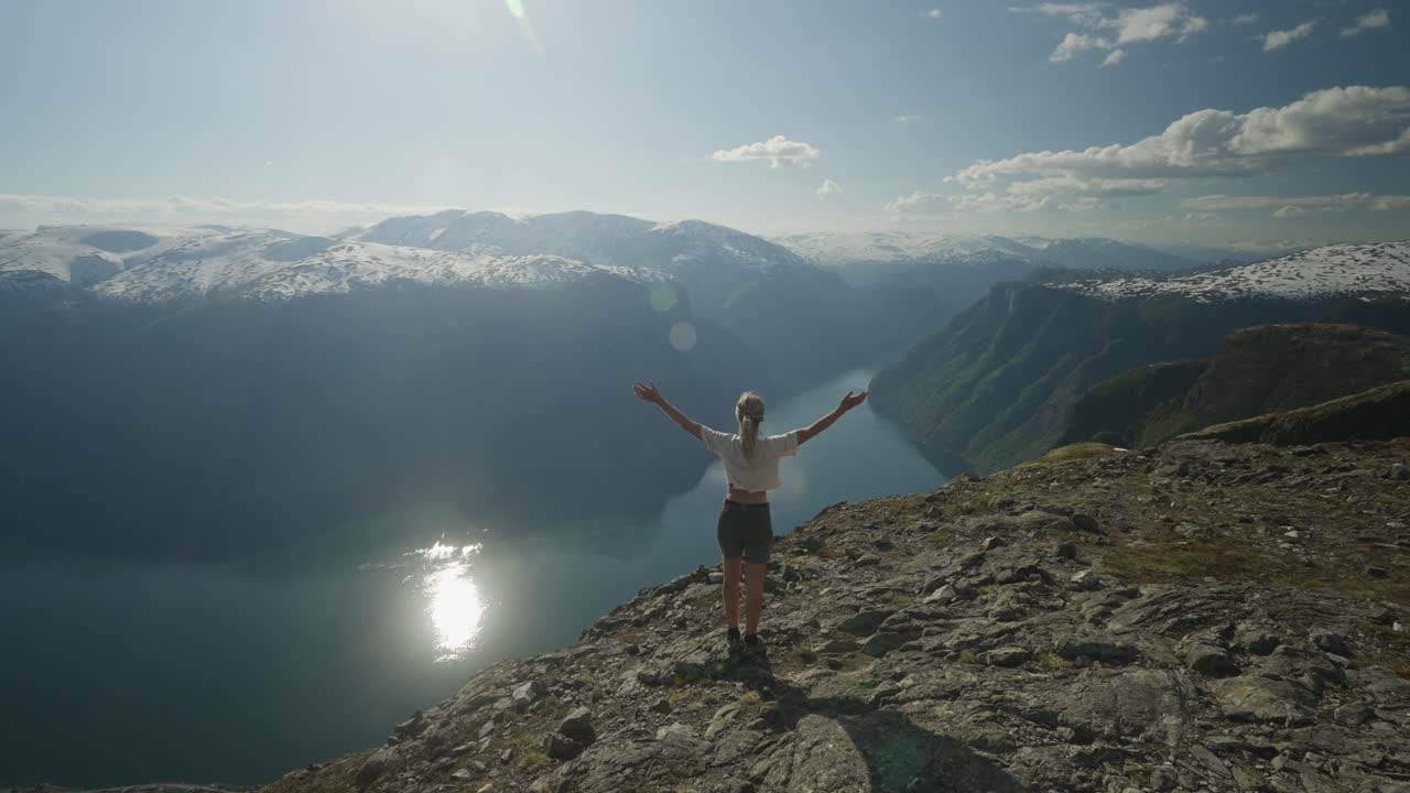 una mujer camina hacia el borde en el monte prest en noruega, admirando la impresionante vista de la montaña y el fiordo