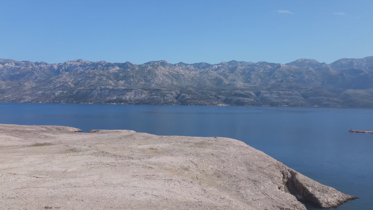 Forward aerial footage of a sun scorched stoney island Pag in Croatia with Velebit mountain in the distance