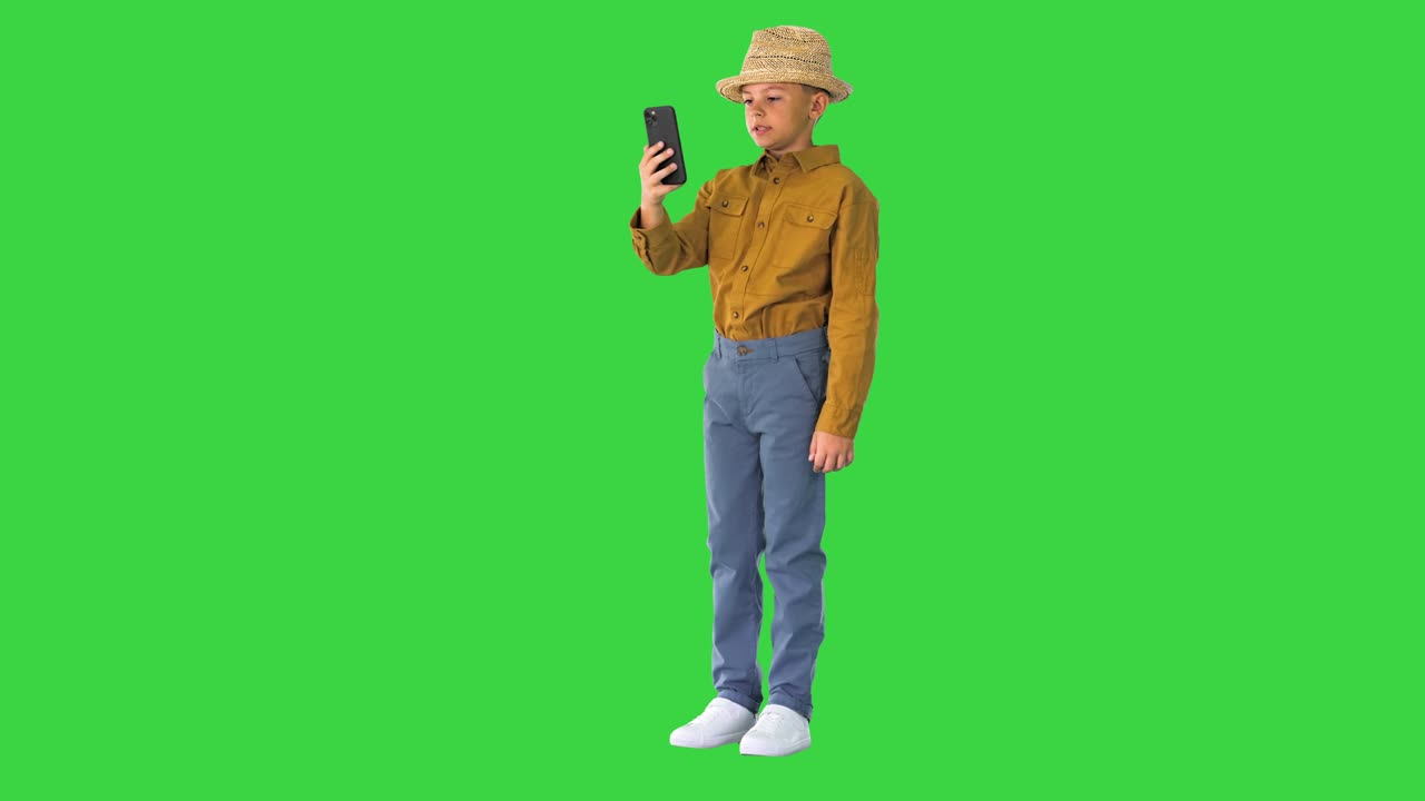 Bambino piccolo con un cappello di paglia che mostra i dintorni mentre è in videochiamata al telefono su schermo verde, Chroma Key