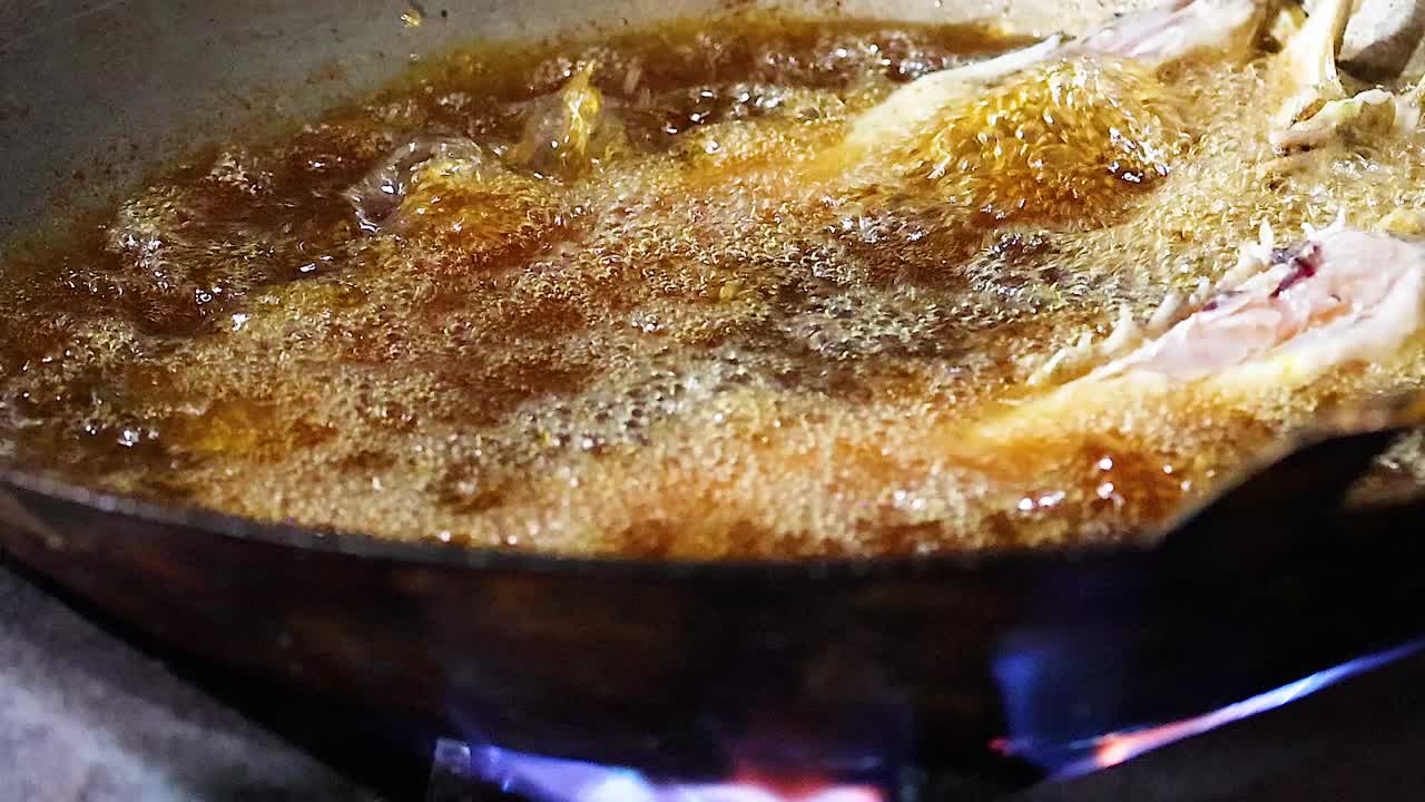 Detailed view of fish sizzling in bubbling oil over a blue flame in a pan.