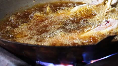 detailed view of fish sizzling in bubbling oil over a blue flame in a pan.