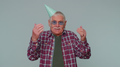 cheerful positive senior man in cone festive hat, dancing, having fun, celebrating birthday party