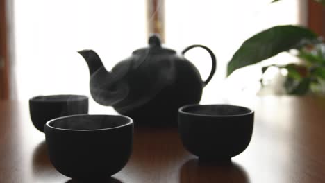 minimal background of a green japanese tea set with steam coming out of the cups, on a wooden table, with a plant and a window in the back