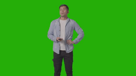 studio shot of casually dressed young man with remote control flicking through tv channels against green screen 1