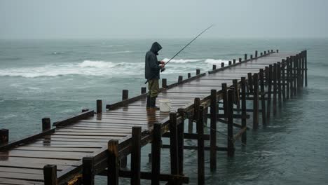 a person fishing on a pier during an overcast or rainy day