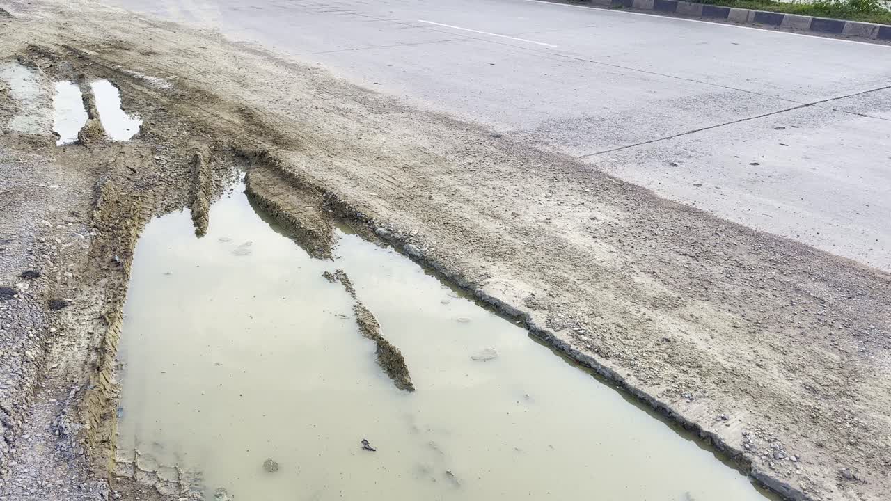 Close-up shot of a damaged highway section with muddy potholes filled with stagnant rainwater near the roadside