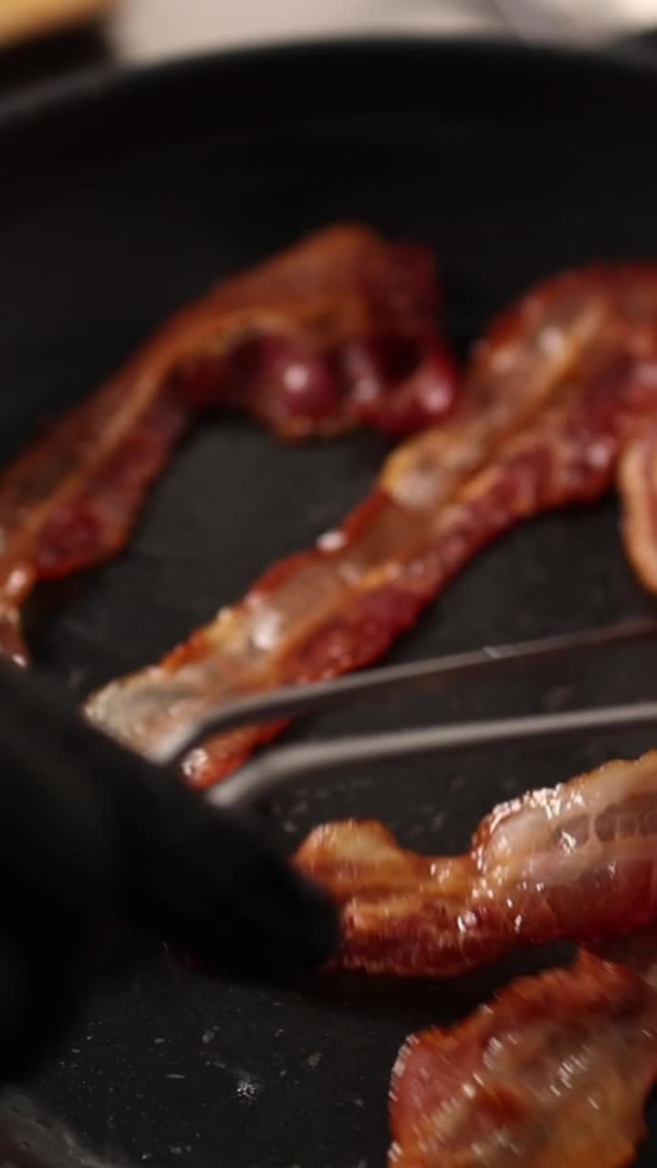 Primo piano di strisce di pancetta che friggono in una padella calda