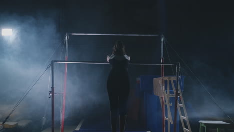 en cámara lenta en el humo chica acróbata en la barra transversal realiza rotación y salto con un golpe. competiciones en gimnasia.