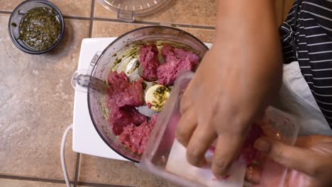 placing ground lamb meat into a food processor to mix in with herbs - overhead view lamb patty series