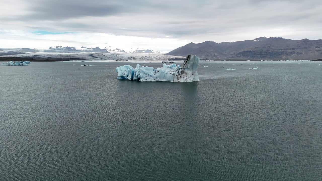 Aerial view of a massive iceberg floating in Jökulsárlón Glacier Lagoon, Iceland, highlighting the icy blue waters, surrounding glaciers, and serene Arctic scenery