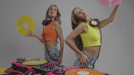 identical twin female djs dancing behind turntables and fanning themselves with records