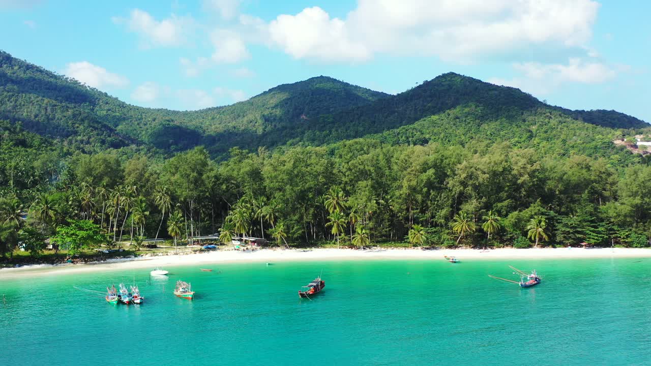Barcos de pesca fondeando en aguas tranquilas y cristalinas de una laguna turquesa poco profunda cerca de una playa de arena blanca de una isla tropical con palmeras y vegetación exuberante.