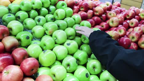 hand reaching for apple among green and red apples