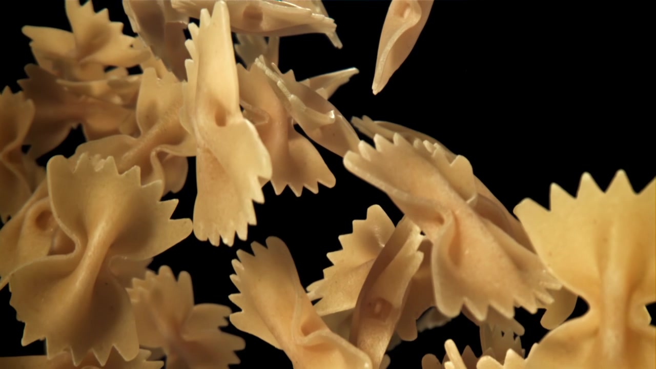 Pasta Farfalle cruda che cade e galleggia al rallentatore su sfondo nero