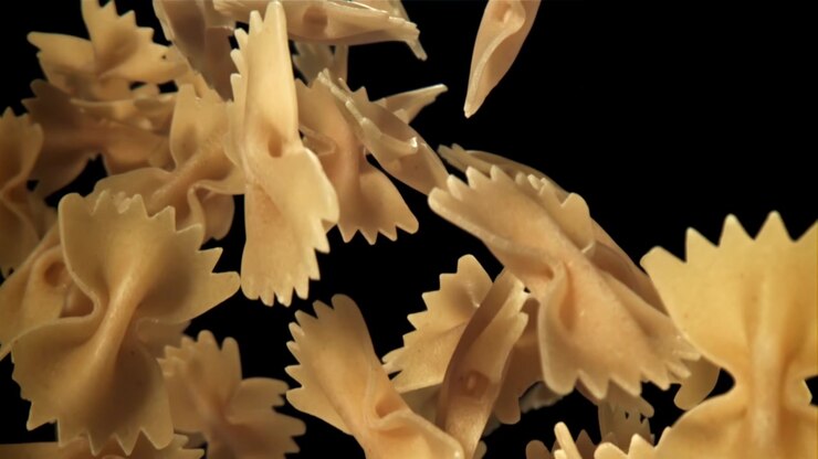 Pasta Farfalle cruda che cade e galleggia al rallentatore su sfondo nero