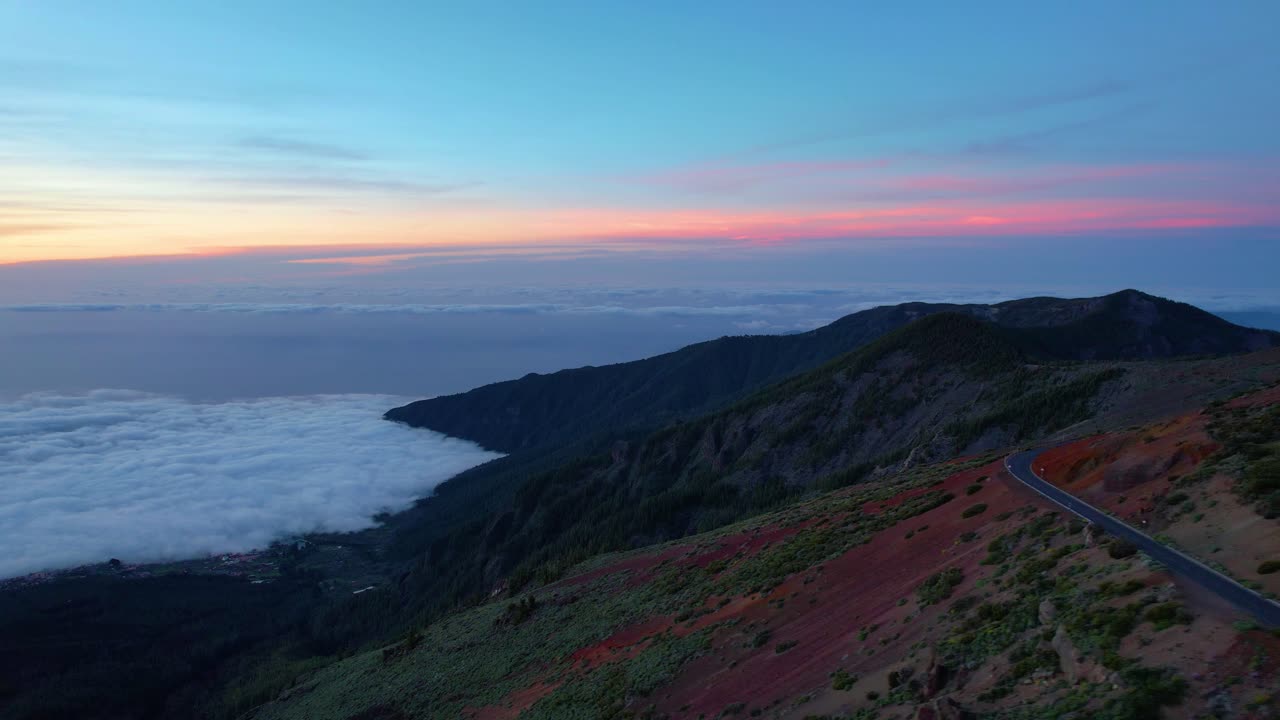 puesta de sol sobre una carretera de montaña con espesas nubes blancas y cielo naranja