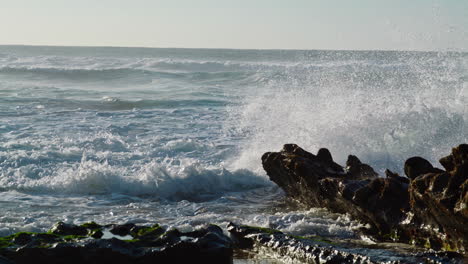 stormy waves crashing rocks on sunny day. dangerous ocean splashing foaming