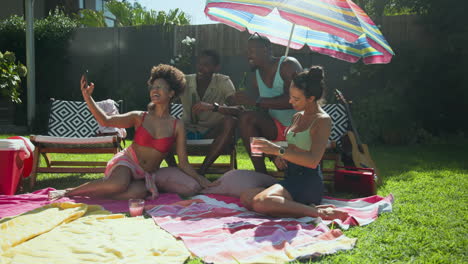 diverse friends relaxing by pool, taking selfies and enjoying drinks under colorful umbrella