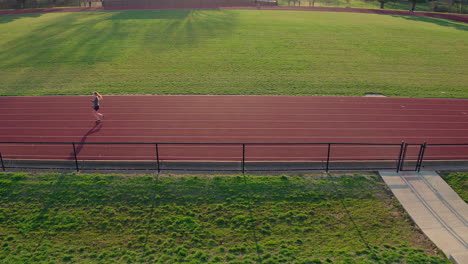 A-teen-girl-athlete-warms-up-at-the-track-at-sunset-camera-pulls-away