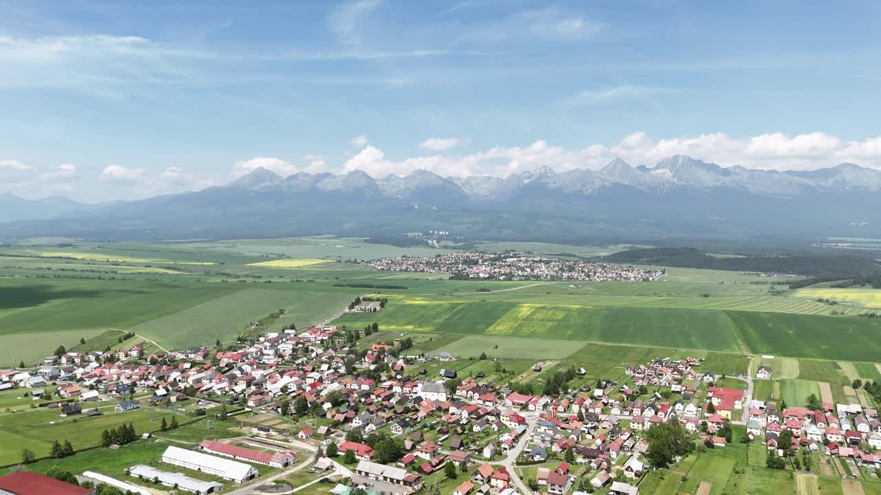 The drone glides sideways over the Slovak countryside, passing green fields and meadows with a distant view of the majestic High Tatras under a clear summer sky