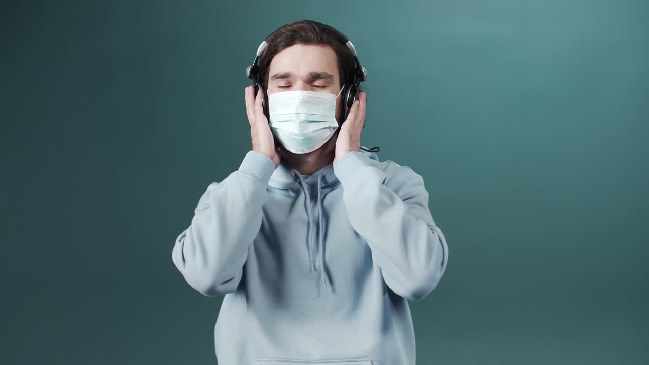 의료 보호 마스크를 입은 예쁜 백인 젊은이가 음악을 듣고 머리를 흔들고 있습니다.