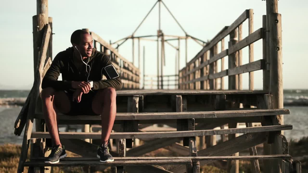 hombre usando reloj inteligente mientras está sentado en las escaleras del paseo marítimo