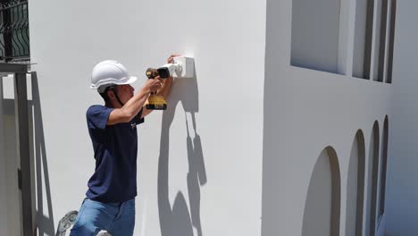 man installing a security camera on the exterior of a white building
