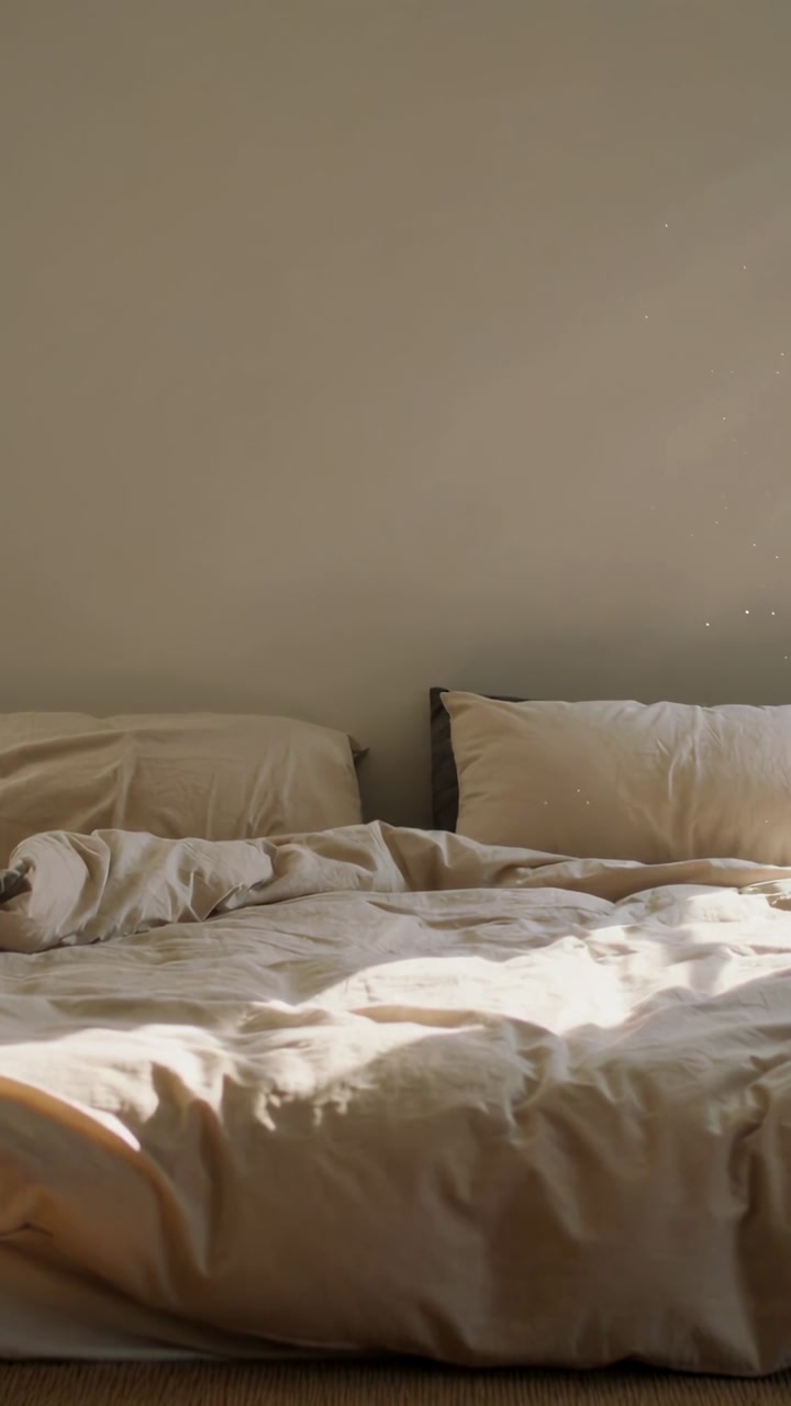 Vertical video: Sunlight entering from left shifting across beige duvet, showing passage of minutes