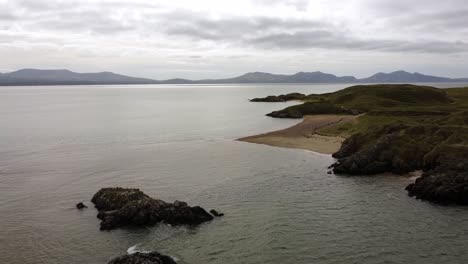 Vista-Aérea-De-La-Playa-Costera-Galesa-De-La-Isla-De-Llanddwyn-Con-Montañas-De-Snowdonia-Al-Otro-Lado-Del-Mar-Irlandés