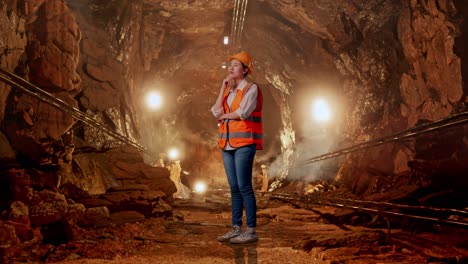 full body side view of asian female engineer with safety helmet thinking and looking around then raising her index finger in underground mine tunnel