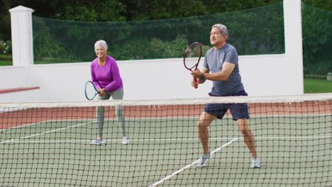 video de una feliz pareja de alto nivel biracial durante el entrenamiento en la cancha de tenis
