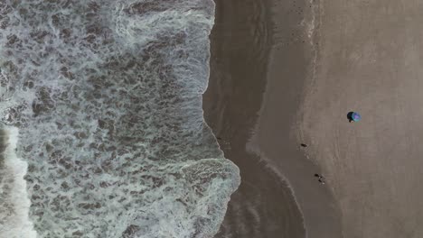 Top-down-shot-of-people-walking-along-the-sand-with-waves-crashing-beside