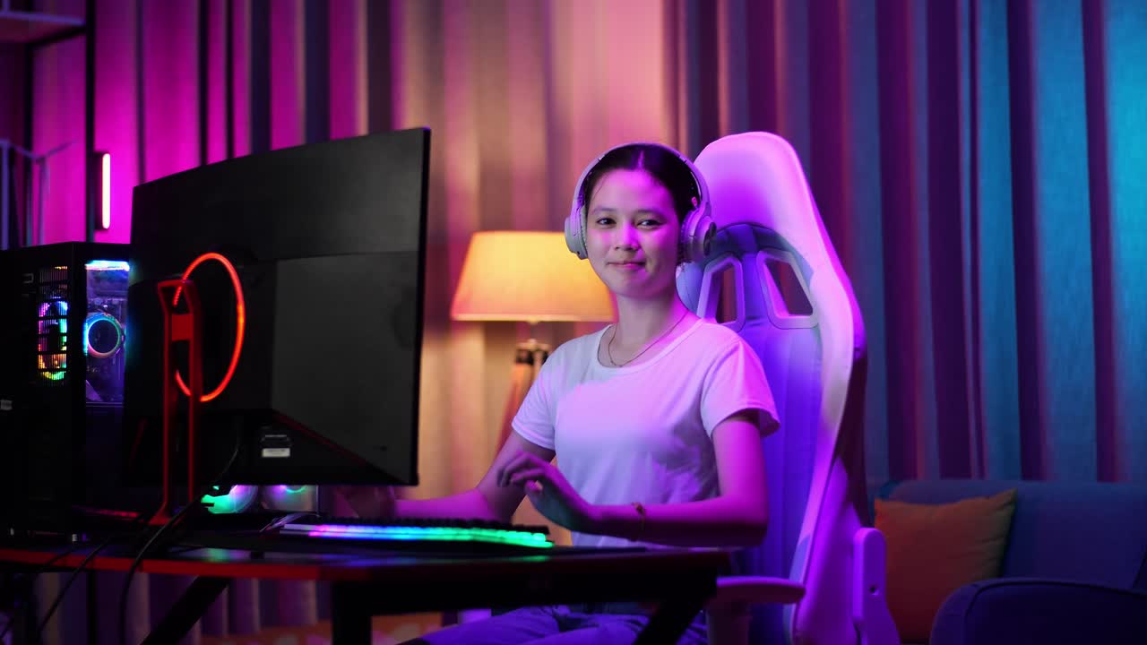 una adolescente asiática sonriendo a la cámara con los brazos cruzados mientras juega un videojuego en la computadora