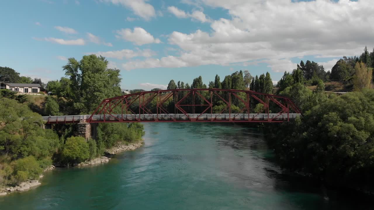 cámara lenta - antena - puente rojo sobre el hermoso río azul en clyde, otago central, nueva zelanda con ciclistas en bicicleta