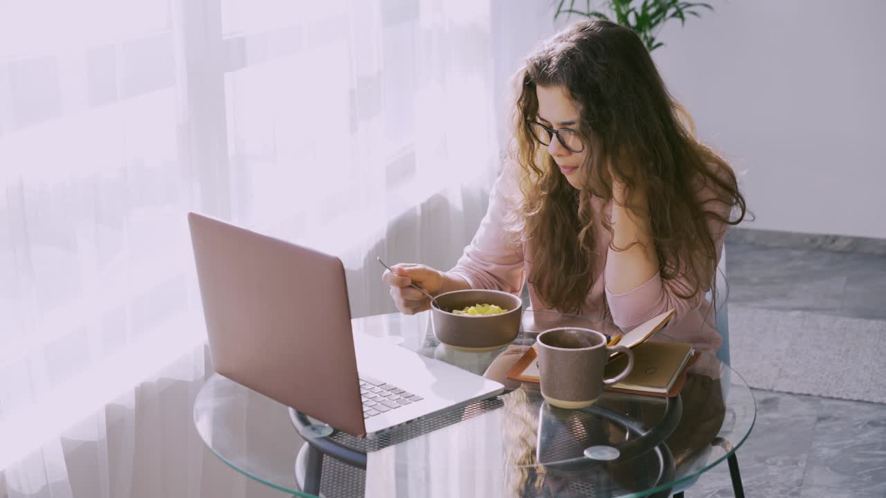 una mujer bonita tiene el desayuno mirando en la computadora portátil en una mesa pequeña