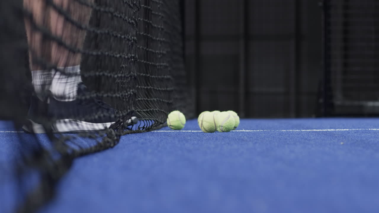Spotting tennis balls, male padel player scooping them with black racket on blue turf, copy space