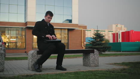 businessman in black coat seated outdoors, struggling to open his briefcase with background of modern urban building, professional, busy, corporate setting in city environment