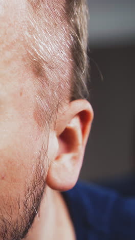 cu shot: nervous young man with blue eyes shaves head using modern electrical trimmer in brightly lit room during quarantine time extreme close view