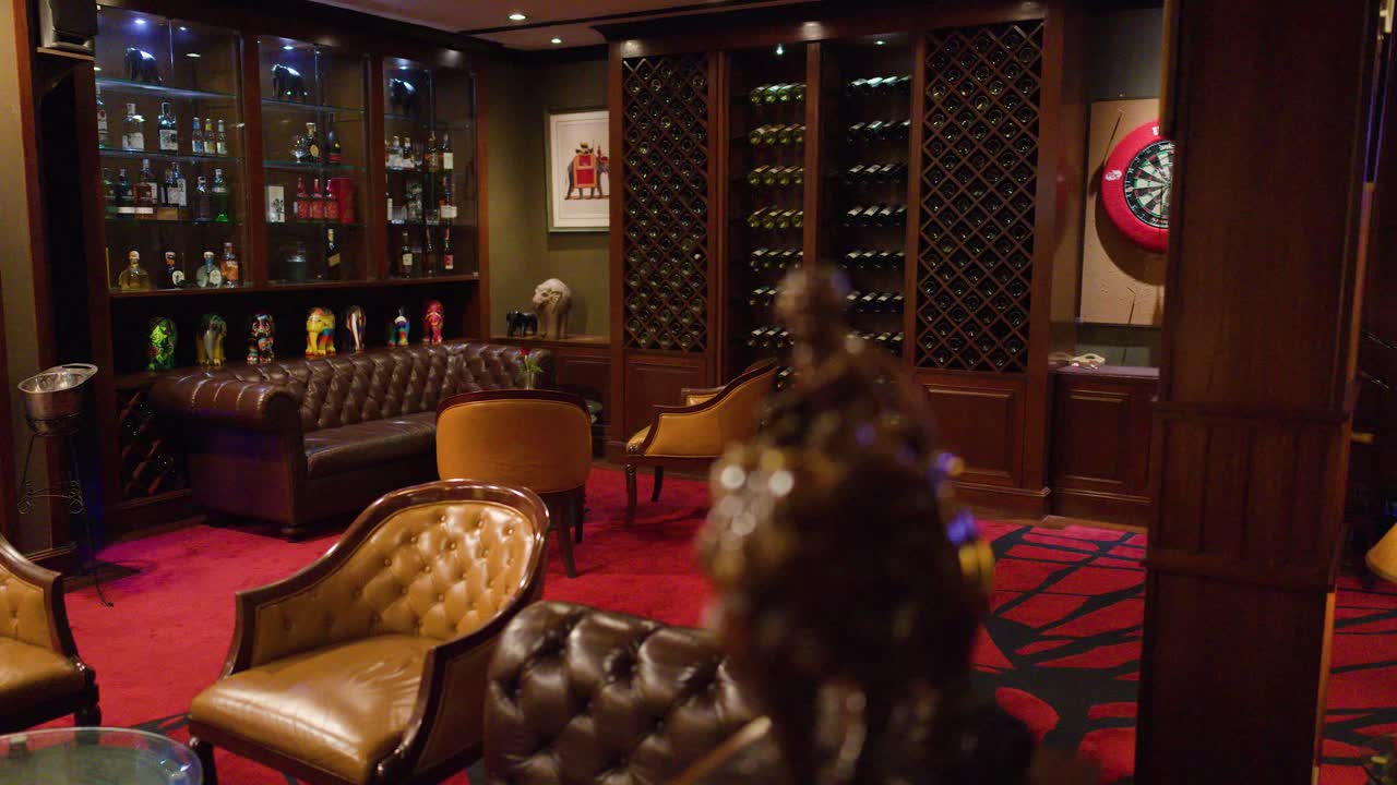 Luxurious lounge bar with leather armchairs, whiskey shelves, warm lighting, and slow camera pan