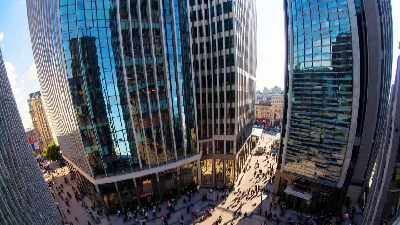 Fisheye video shot of a bustling city plaza surrounded by towering skyscrapers
