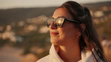 rostro de una joven caucásica con gafas de sol disfrutando de la brisa del mar al atardecer