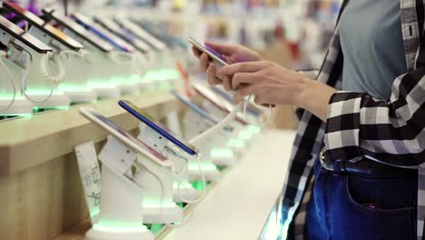 waist shot of unrecognizable woman's hands chooses a smartphone in and electronics store. she takes smartphone from counter and