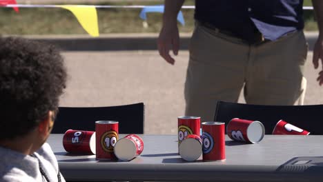 young children throwing bean bag at tin cans in slow motion