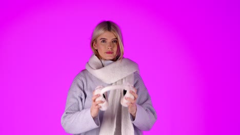 una mujer rubia bonita quitándose los auriculares de invierno, elegante ropa de invierno gris, retrato de estudio