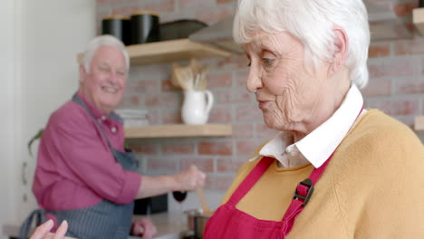 Senior-caucasian-couple-cooking-dinner-using-tablet-in-kitchen-at-home,-slow-motion