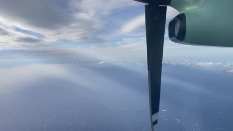 domestic aircraft norway, turboprop engine, filmed out of window above arctic northern norway, with snow capped mountings, beams of light, and clouds, lofoten island in the background,tilt upward shot