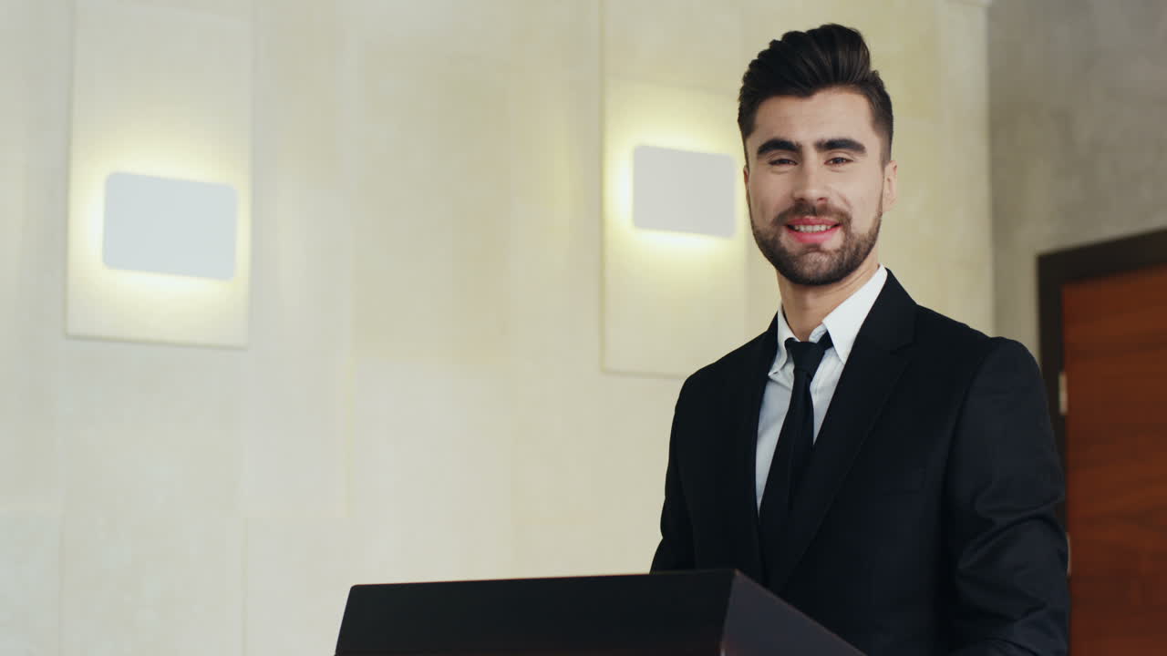 vista de primer plano joven hombre de negocios caucásico con ropa formal en un podio mirando a la cámara y sonriendo en una sala de conferencias