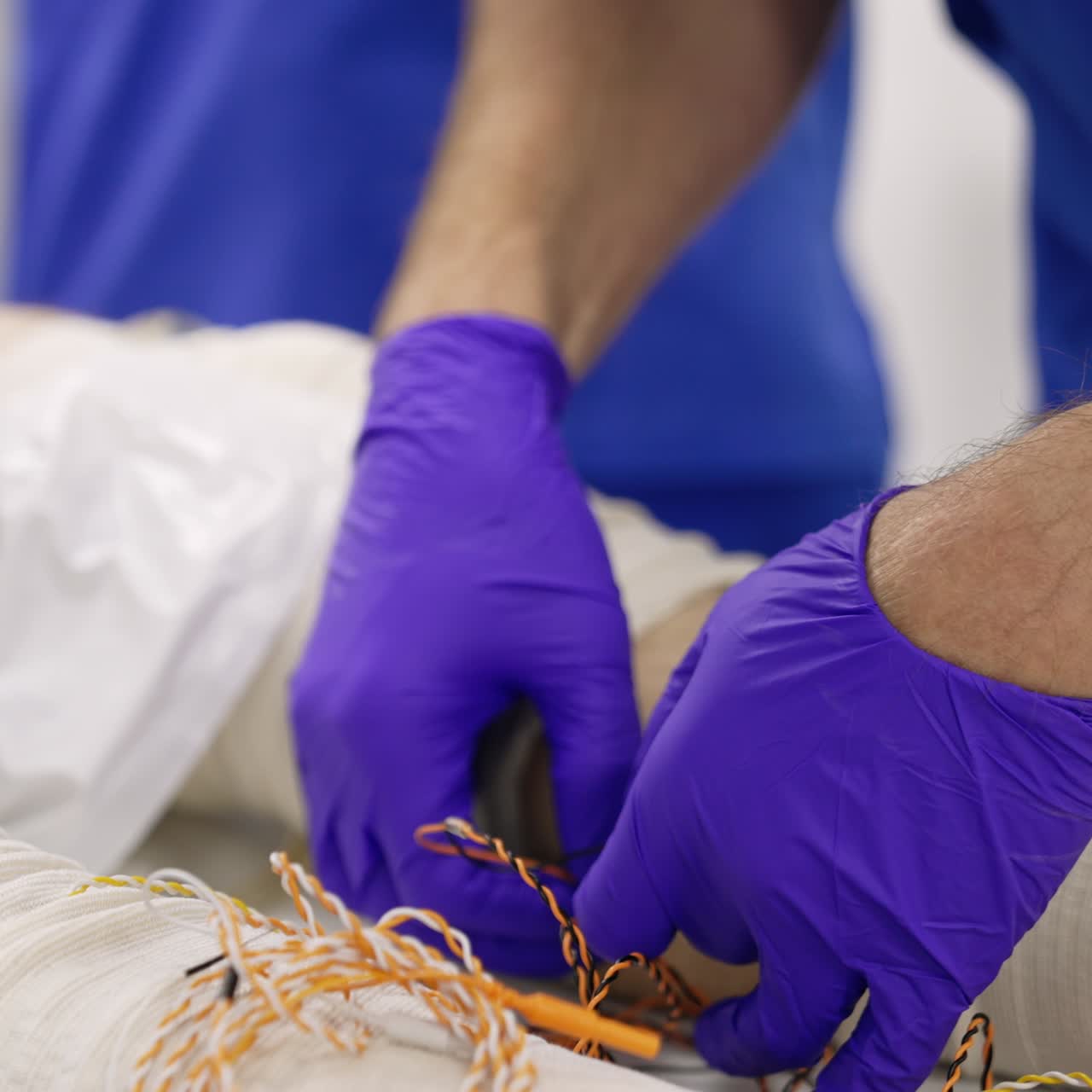 Doctor's hands in latex gloves attaching thin wires to the patient's legs. Getting ready for the neuromonitoring procedure in clinics